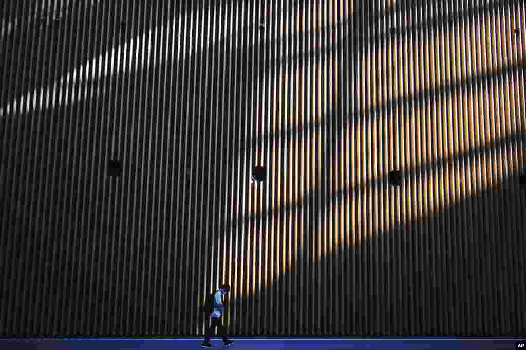 A man with a protective face mask to protect against the spread of the coronavirus walks through the shadows of a building in Tokyo.