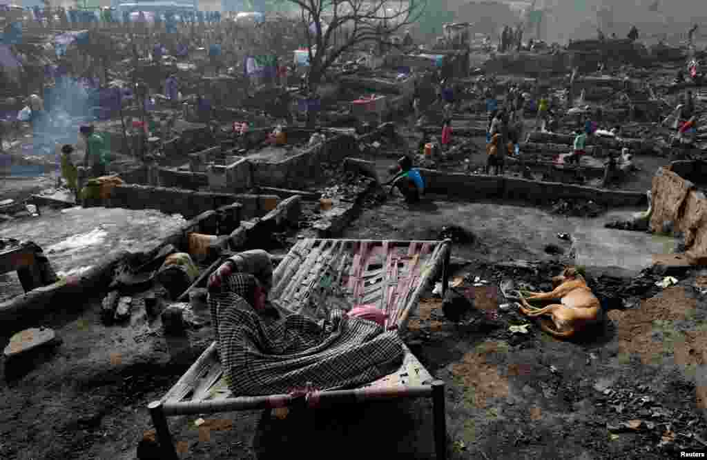 A woman sits on a broken bed with her family dog on the floor of a burnt-out house as people search for their belongings after a fire broke out in a slum in Karachi, Pakistan, Jan. 22, 2020.