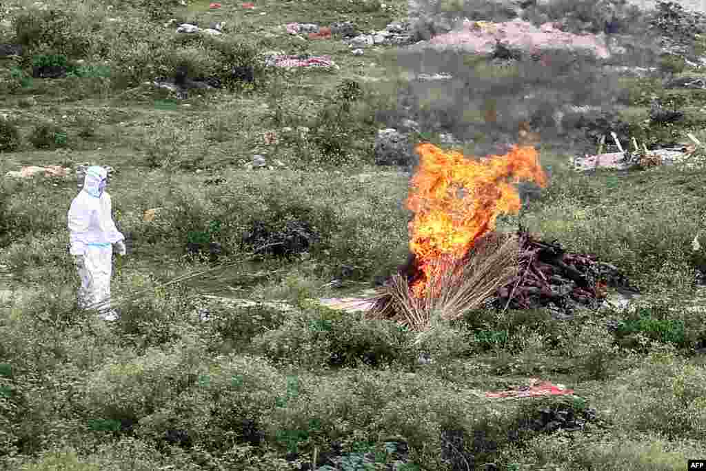 A health worker wearing Personal Protective Equipment (PPE) watches the funeral pyre of a man, who died from the COVID-19 coronavirus, at Phaphamau Ghat near the River Ganges in Allahabad, India.