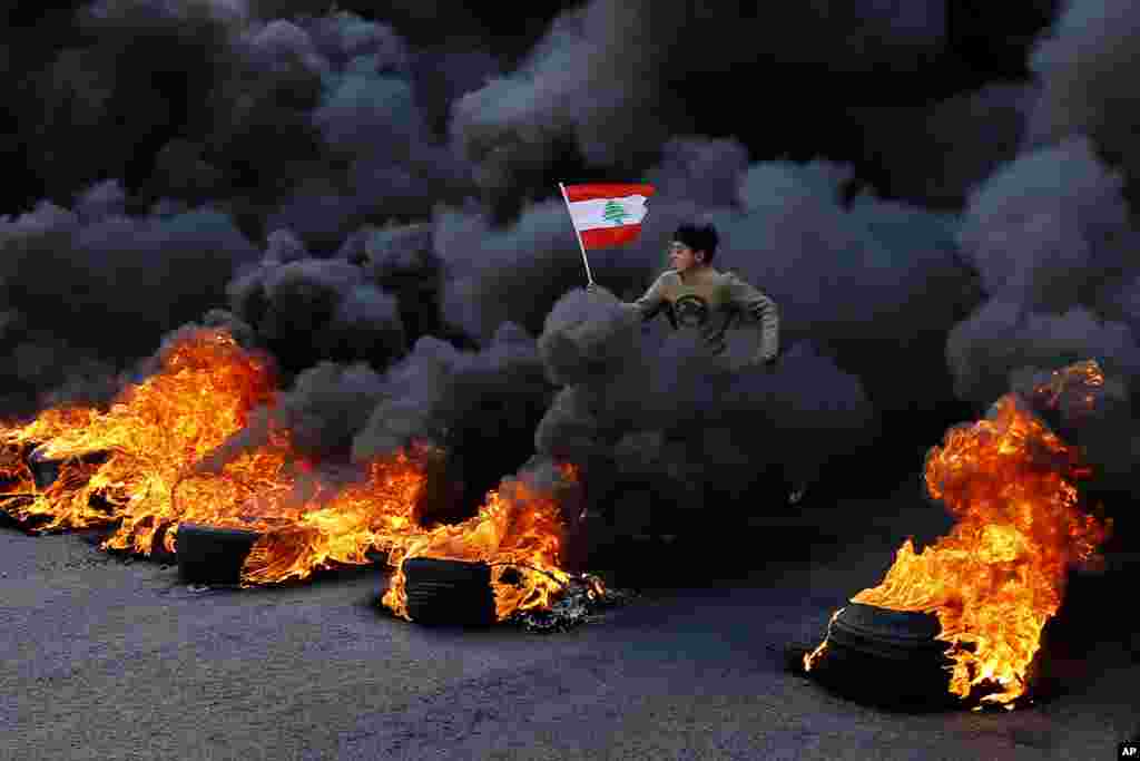 An anti-government demonstrator jumps over tires set on fire to block a main highway during a protest in the town of Jal el-Dib, north of Beirut, Lebanon.