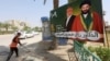 A worker cleans the street next to a campaign poster of candidates ahead of the parliamentary election, in Najaf, Iraq, April 14, 2018.