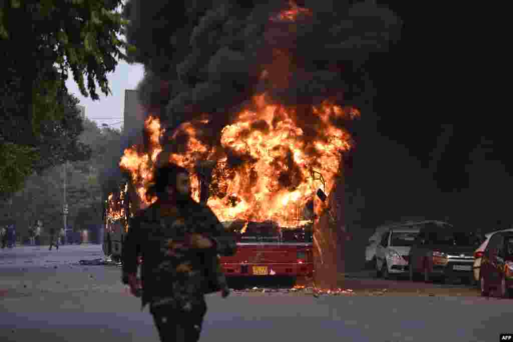 A man walks on a street as a bus is on fire following a demonstration against the Indian government's Citizenship Amendment Bill (CAB) in New Delhi.
