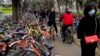 Residents ride bicycles from bike-sharing company Ofo try to pedal through a sidewalk crowded with bicycles from the bike-sharing companies Ofo, Mobike and Bluegogo, near a bus stand in Beijing, China, March 23, 2017. As many as 2.2 million of these two-w