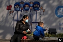 2021年11月17日, 在北京前門街道的一幅抗疫宣傳畫下，一名幼兒在一名女子的看顧下玩耍。（美聯社)