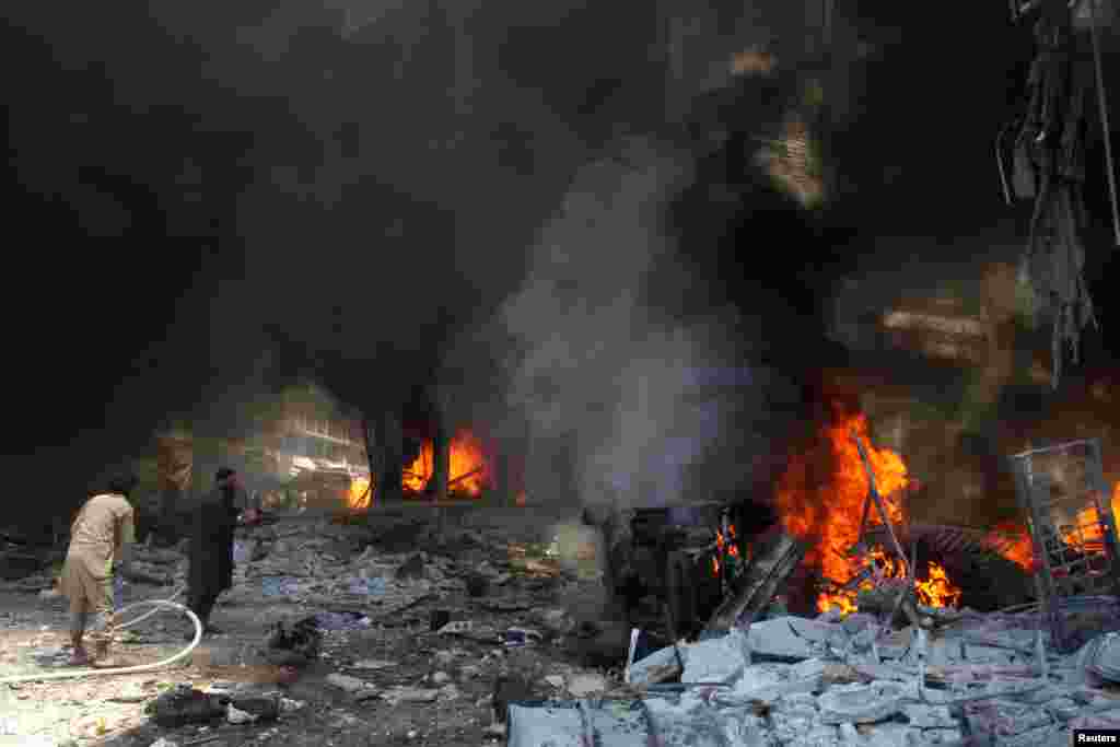 Warga Suriah berusaha memadamkan api pasca serangan udara pasukan Suriah terhadap sebuah pasar di Idlib.