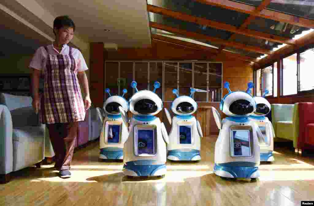 Seorang pekerja perempuan melewati robot-robot yang "bekerja" di rumah perawatan jompo di Hangzhou, Zhejiang, China.