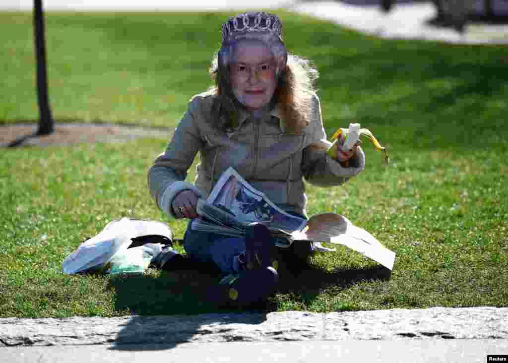 A woman wearing a mask of Britain's Queen Elizabeth reads a newspaper near Tower bridge in London.