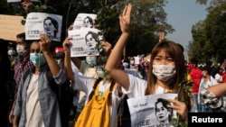 緬甸仰光的示威者致象徵反政變抗議的三指禮，另一隻手拿著緬甸國務資政昂山素姬的畫像，要求軍政府釋放這位諾貝爾和平獎得主。