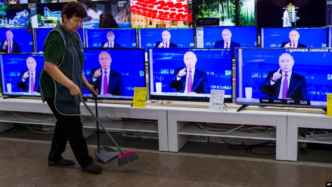 A cleaner walks past a store in Moscow with TV sets showing Russian President Vladimir Putin during his annual live call-in show, June 15, 2017.