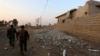 FILE - Peshmerga fighters walk past a damaged house in an Iraqi Kurdish Kakai minority village located near the town of Kalak, east of Mosul, Oct. 26, 2016.