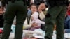 Una mujer sostiene su pulsera para mostrar a los agentes de la Patrulla Fronteriza de EEUU que ella y su hija han estado esperando más tiempo entre dos muros fronterizos para solicitar asilo, el viernes 12 de mayo de 2023, en San Diego. (Foto AP/Gregory Bull)