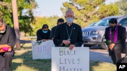 In this June 1, 2020, photo provided by the Catholic Diocese of El Paso, Bishop Mark Seitz, center, kneels with other demonstrators at Memorial Park holding a Black Lives Matter sign in El Paso, Texas.