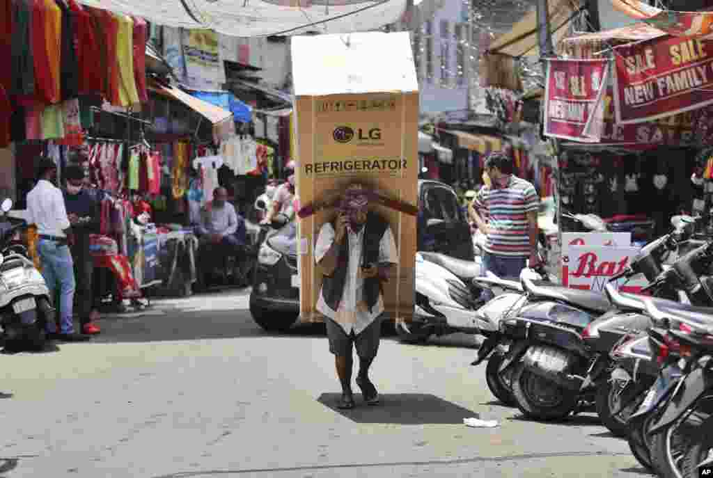 An Indian laborer talks on his mobile phone as he transports a refrigerator on his back at a market in Jammu.