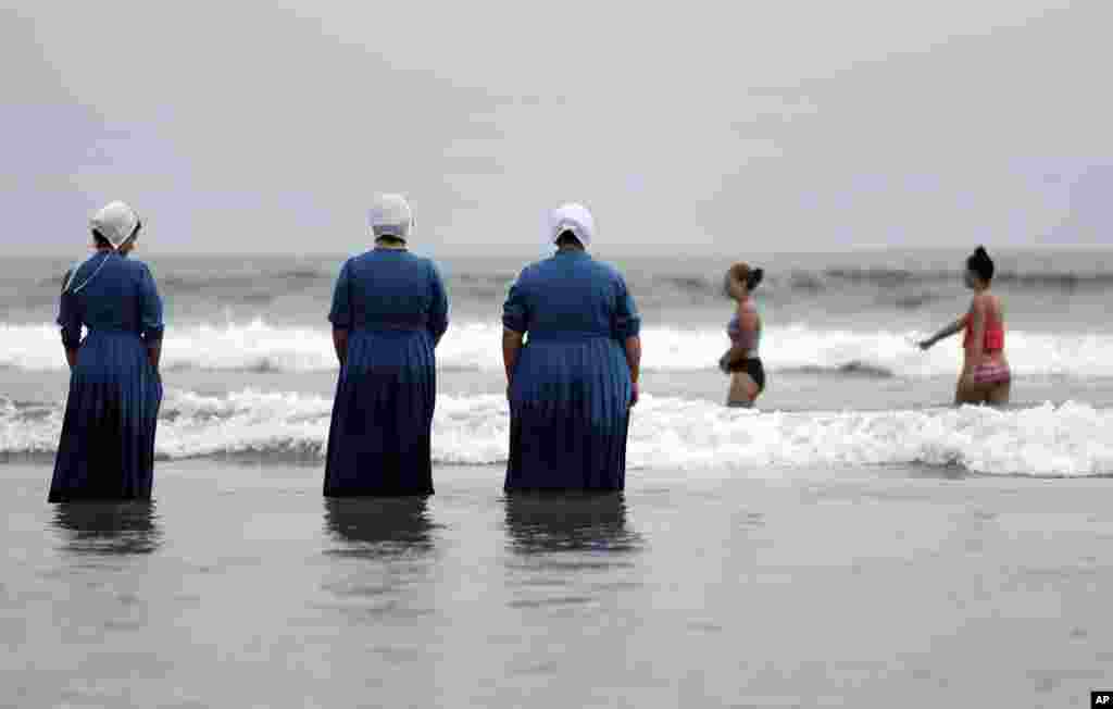 Tiga perempuan dari komunitas Amish di Michigan (membelakangi kamera), melakukan perjalanan pertama ke pantai di Lautan Pasifik di kota Coronado, California.