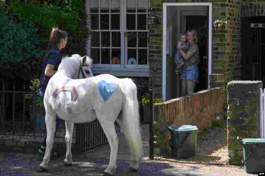 Bryony Blant holding her daughter Alice, who celebrates her 2nd birthday, look at Welsh mountain pony Annie's Wizz held by handler Daisy Cinque outside their home in Twickenham, south west London. Park Lane Stables are taking the fun to peoples' windows during the novel coronavirus lockdown in an initiative called "Tiny pony at your window."