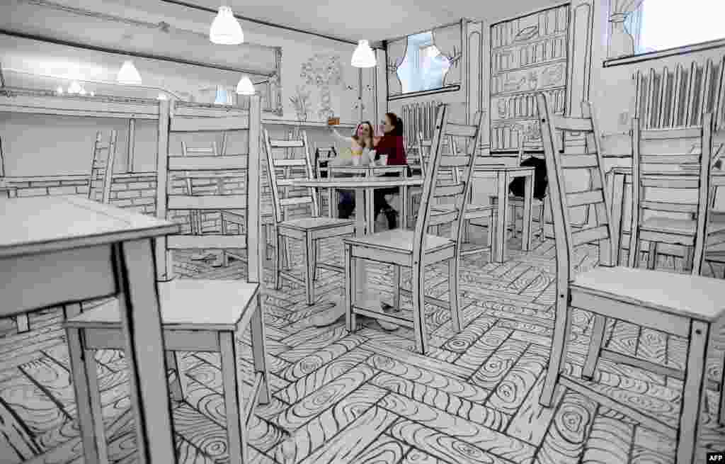 Two young women take a selfie picture at the B&W cafe with a black and white interior in St. Petersburg, Russia.