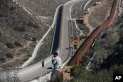 A man looks out at the U.S. border where workers are replacing parts of the U.S. border wall for a higher one, in Tijuana, Mexico, Dec. 19, 2018.