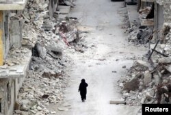 A woman walks past damaged buildings in the rebel-controlled area of Maaret al-Numan town in Idlib province, Syria, May 13, 2016.