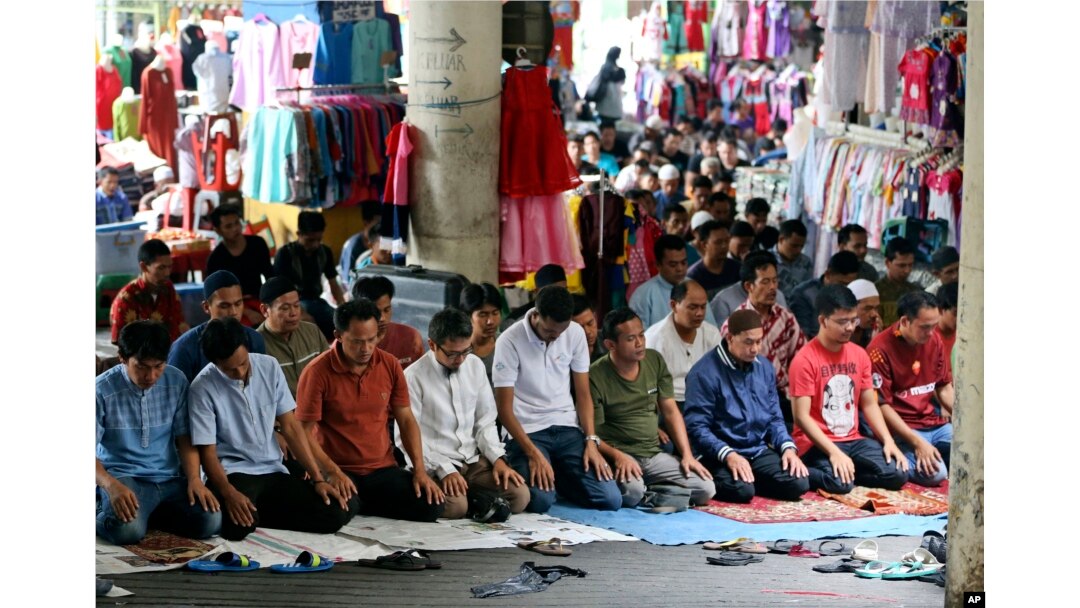 Muslim men perform Friday prayer amid clothing displayed at fashion stalls in Tanah Abang market in Jakarta, Indonesia, Friday, June 2, 2017