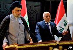 FILE - In this photo provided by the Iraqi government, Iraqi Prime Minister Haider al-Abadi, right, and Shiite cleric Muqtada al-Sadr hold a press conference in the heavily fortified Green Zone in Baghdad, Iraq, May 20, 2018.