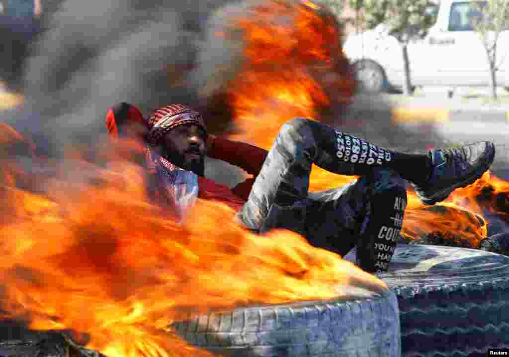 An Iraqi demonstrator sits amid burning tires blocking a road during ongoing anti-government protests in Najaf.