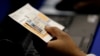 FILE - An election official checks a voter's photo identification at an early voting polling site in Austin, Texas.