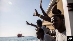 Migrants aboard the Open Arms aid boat, of Proactiva Open Arms Spanish NGO, react as the ship approaches the port of Barcelona, Spain, Wednesday, July 4, 2018. The aid boat sailed to Spain with 60 migrants rescued on Saturday in waters near Libya, after it was rejected by both Italy and Malta.