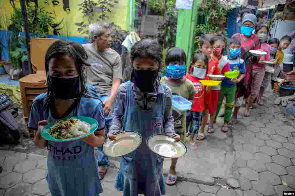 Locals wearing protective masks carry plates while queueing for food distributed for free amid the spread of coronavirus disease (COVID-19) in Bandung, West Java province, Indonesia.