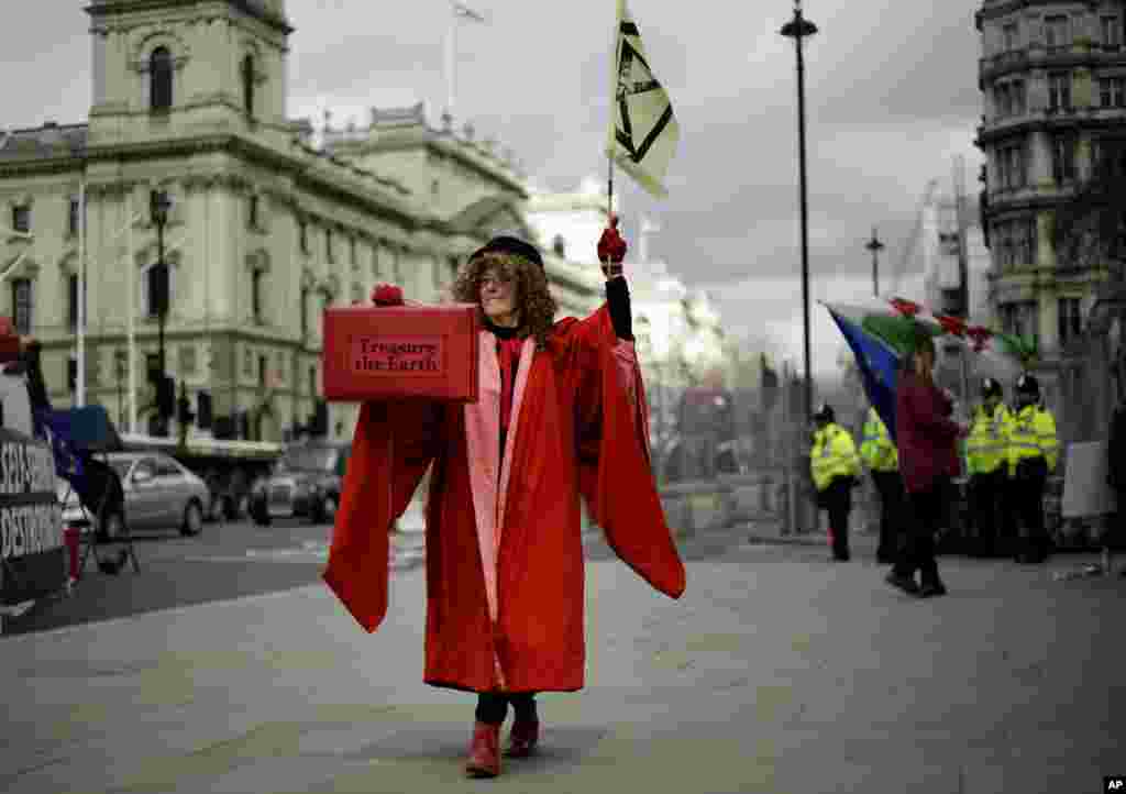 A woman dressed as the Speaker of the House of Commons holds a case with a message 'treasure the earth' as she participates in a demonstration on the budget outside Parliament in London.