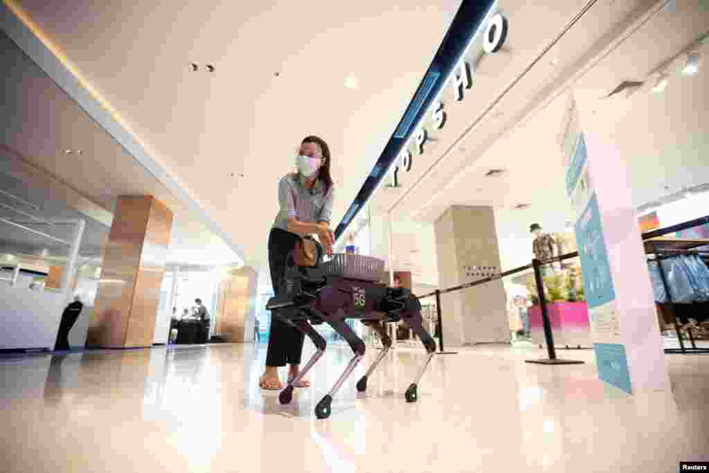 A woman uses hand sanitizer gel from a four-legged dog robot called "K9" at the Central World department store, after the Thai government eased isolation measures to prevent the spread of the COVID-19 in Bangkok, Thailand.