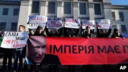 Protesters hold posters reading: "We will never surrender!" "Donbass is Ukraine!" and a banner "The empire must die" in front of Russian Embassy in Kyiv, Ukraine, Feb. 22, 2022. (AP/Efrem Lukatsky)