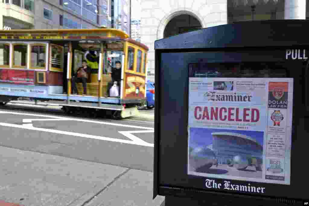 A newspaper headline announcing the closure of large events is displayed as a cable car goes down California Street in San Francisco.