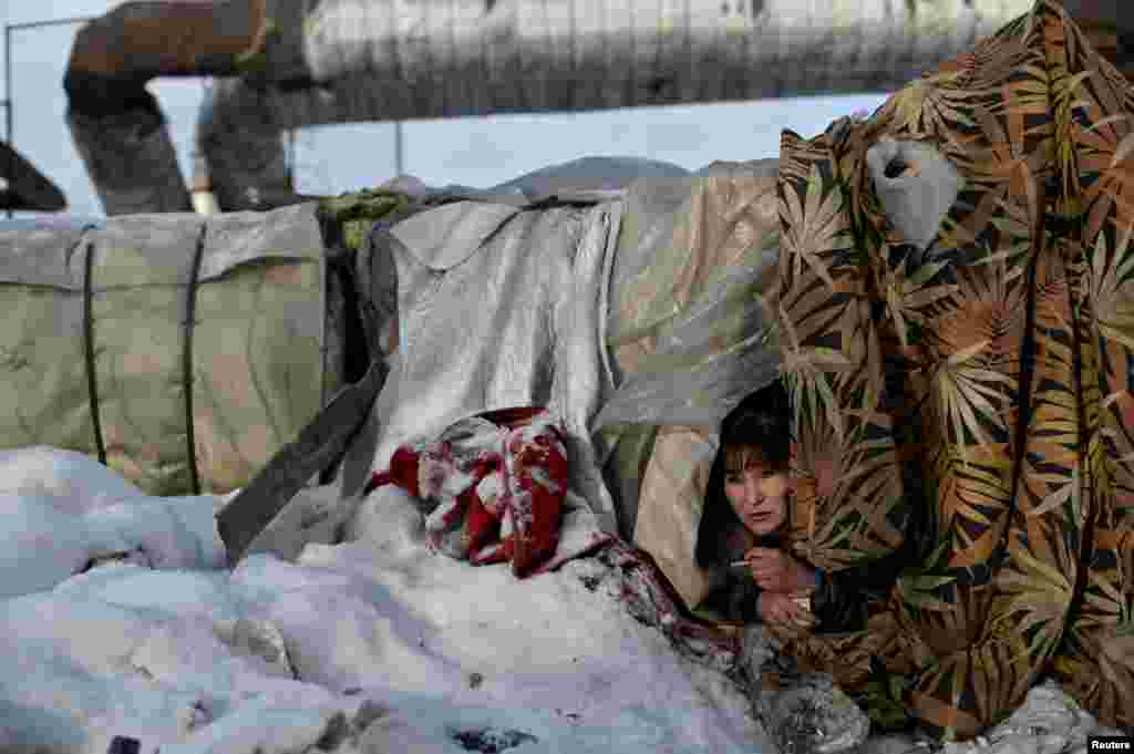 Galiya, 29, who is homeless, looks out from Alexey's makeshift shelter in Omsk, Russia.