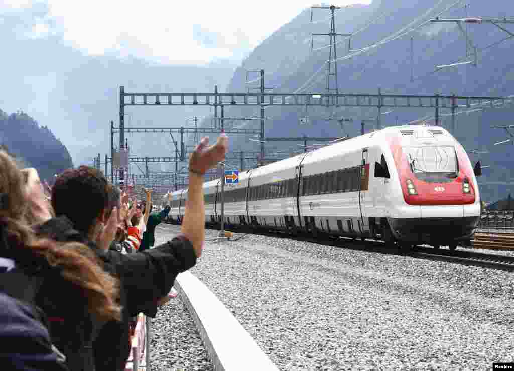 Para tamu melambai ke arah kereta api yang baru saja melalui terowongan kereta terpanjang di dunia 'NEAT Gotthard' sepanjang 57,1-km di bawah pegunungan Alpen di Swiss.
