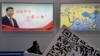 An attendee at a conference looks up near a portrait of Chinese President Xi Jinping with the words "Xi Jinping and One Belt One Road" and "One Belt One Road Strategy," in Beijing, April 28, 2017.