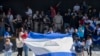 Nicaragüenses residentes en Costa Rica exhiben una bandera nicaragüense durante la llegada de la Miss Universo nicaragüense Sheynnis Palacios al Aeropuerto Internacional Juan Santa María en Alajuela, Costa Rica, el 26 de febrero de 2024. (Foto de Ezequiel BECERRA / AFP)
