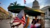 A man pedals his bicycle taxi, decorated with Cuban and U.S. flags, as he transports a woman holding a girl, near the Capitolio in Havana, Cuba, March 15, 2016. 