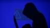 FILE - A hooded man holds a laptop computer as blue screen with an exclamation mark is projected on him in this illustration picture taken on May 13, 2017.