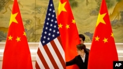 ARCHIVO - En esta fotografía de archivo del 14 de febrero de 2019, empleados chinos ajustan las banderas de Estados Unidos y China antes de la sesión inaugural de negociaciones comerciales entre representantes comerciales de Estados Unidos y China en Beijing. AP