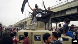 FILE - Islamic State group militants hold up their flag as they patrol in a commandeered Iraqi military vehicle in Fallujah, Iraq, March 30, 2014. The United States Friday sanctioned three members of the Islamic State who were featured in a beheading video distributed by the group and accused of luring recruits in Southeast Asia.