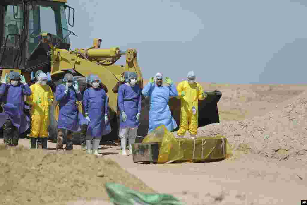 Iraqi health ministry workers pray by a coffin of a person who died from coronavirus at a new cemetery for the people outside the town of Najaf.