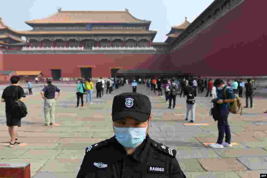 A security guard stands watch as people line up while ensuring social distancing to enter the Forbidden City, the former palace of China's emperors, in Beijing. The area was reopened three months after it closed due to the coronavirus crisis.