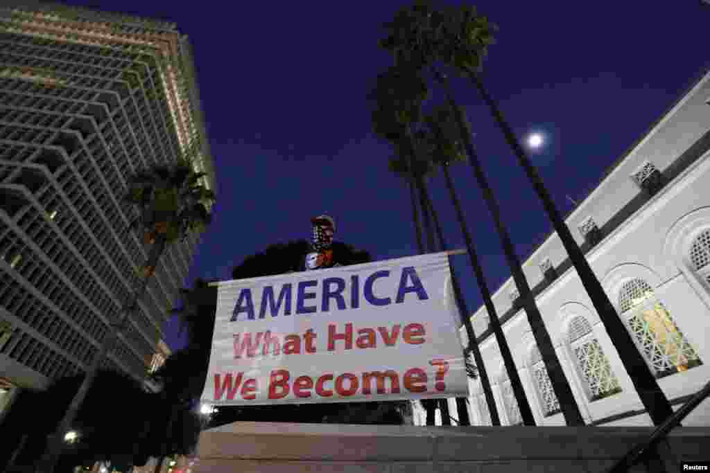 A man holds a sign reading "AMERICA What Have We Become?" during a protest against the impeachment acquittal of U.S. President Donald Trump outside city hall in Los Angeles, California, Feb. 5, 2020.
