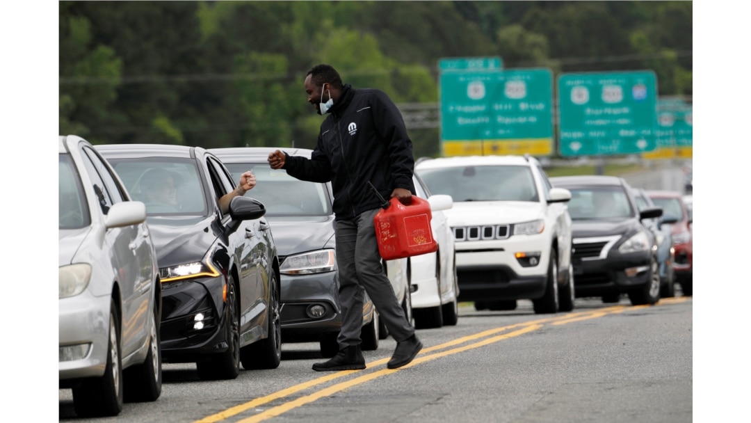 FILE - A man with a gas container greets a motorist waiting in a lengthy line to enter a gasoline station during a surge in the demand for fuel following the cyberattack that crippled the Colonial Pipeline, in Durham, North Carolina, May 12, 2021.