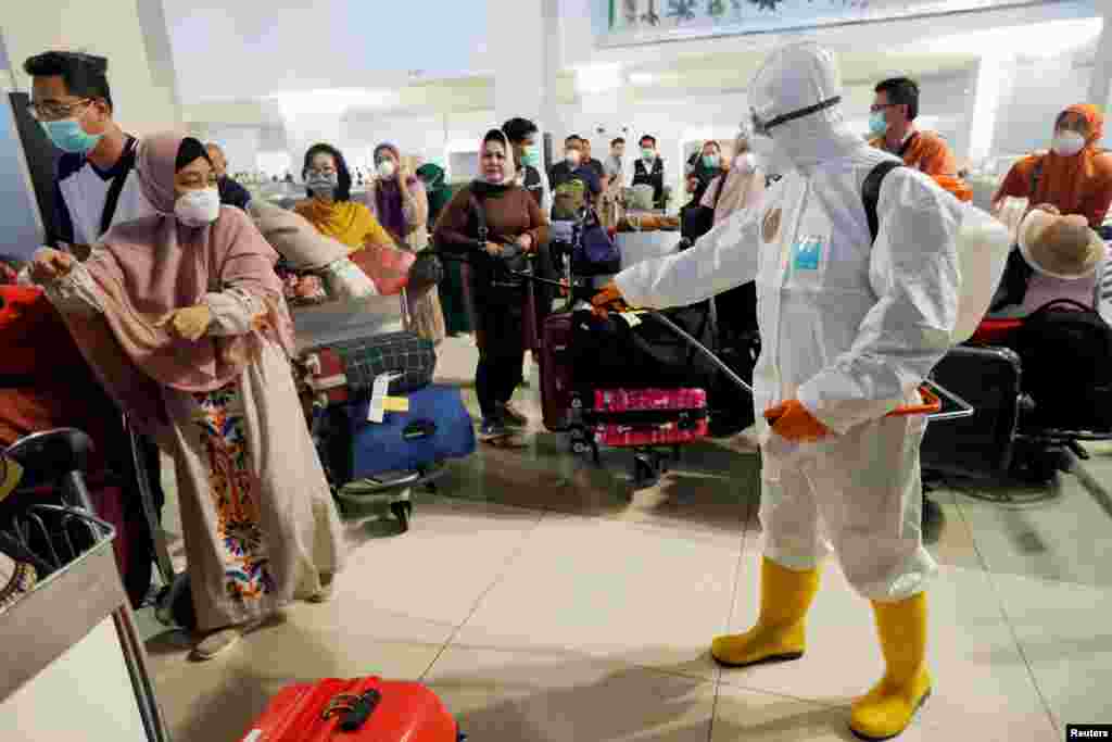 A traveler reacts as a worker sprays disinfectant on passengers' bags at the international arrivals terminal of Soekarno-Hatta Airport near Jakarta, Indonesia, amid the coronavirus outbreak.