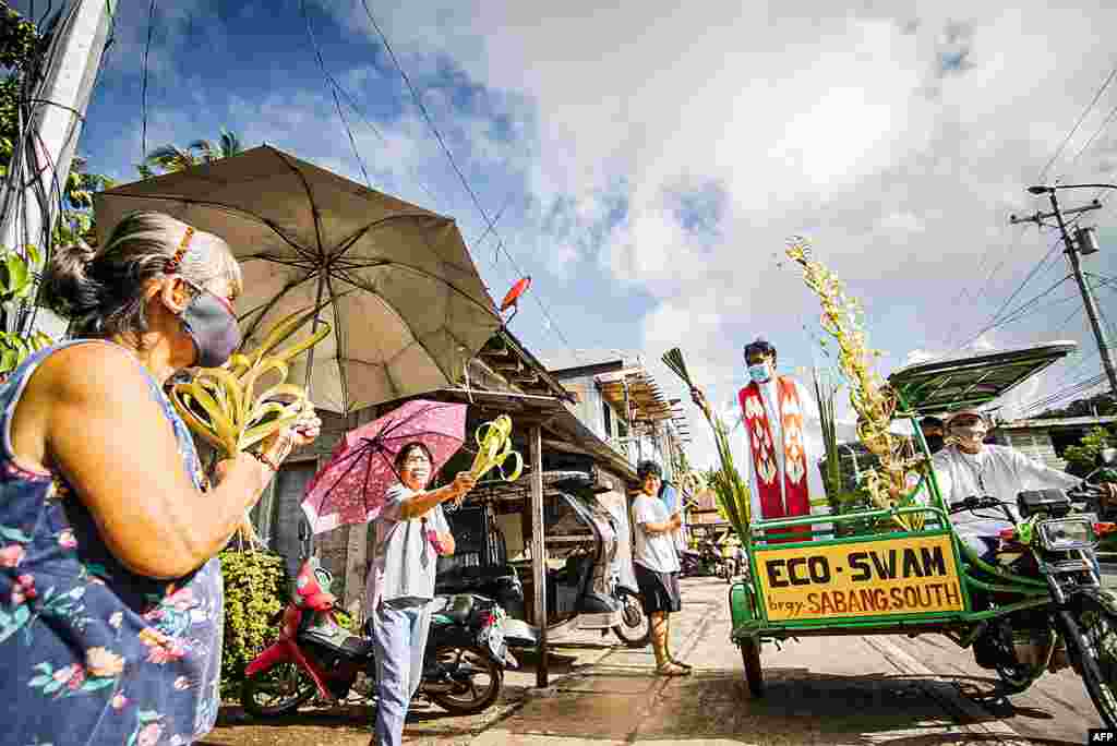 Roman Catholic priest Pepe Quitorio riding on a tricycle and wearing a face mask blesses the faithfuls holding coconut leaves during Palm Sunday event in Borongan town, Eastern Samar province, central Philippine.