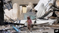 Un niño palestino pasa junto a edificaciones destruidas durante el bombardeo israelí de la Franja de Gaza en Deir al Balah el sábado 13 de enero de 2024.